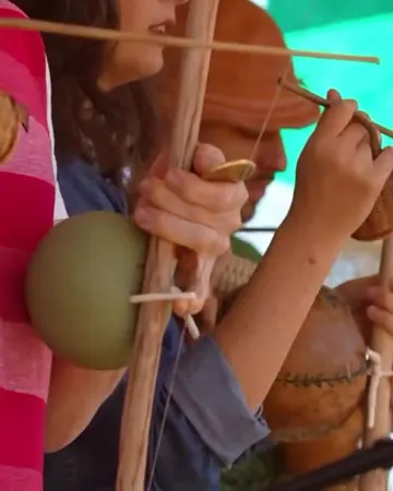 Mãos tocando berimbau, com a cabaça em primeiro plano